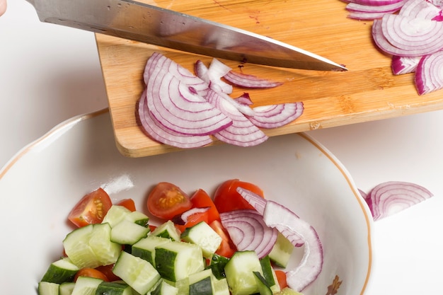 Sliced red onions are transferred to a salad bowl with other vegetables.