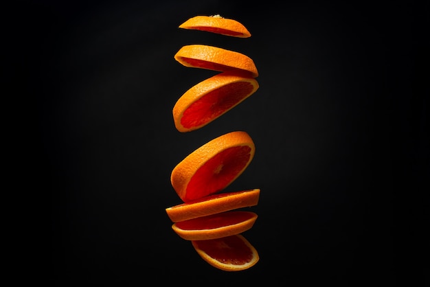 A sliced red orange levitates in the air. Creative photo of flying orange on black background