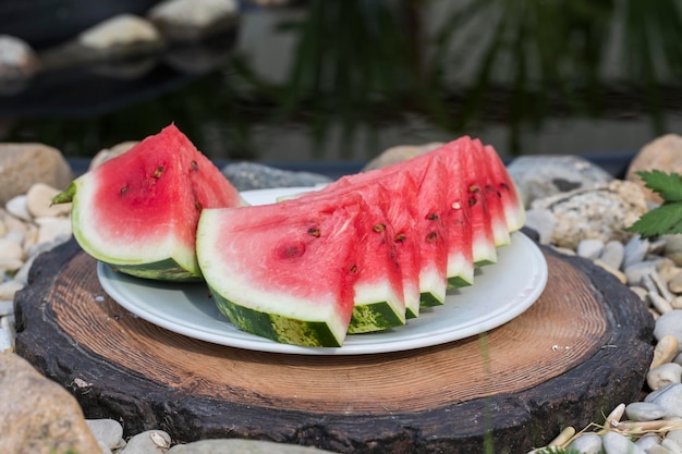 Sliced red watermelon with seeds on a white platter on a stump