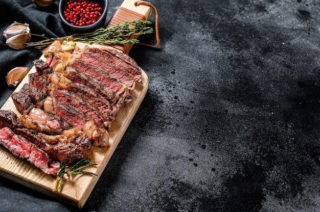 Sliced rib eye steak on a chopping Board, medium rare. top view. Copy space