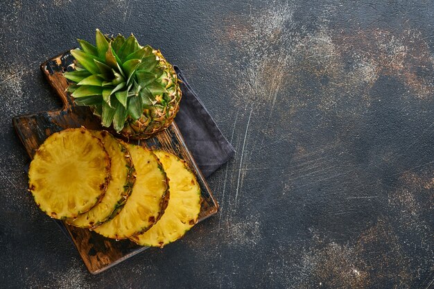 Sliced ripe pineapple on dark brown stone background. Tropical fruits. Top view. Free space for text. Mock up.