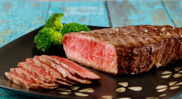 Sliced roasted rare beef sirloin with broccoli on plate.