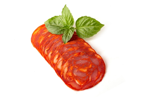 Sliced round pieces of rawcured Chorizo sausage with basil leaf on a white background