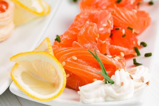 Sliced salmon with sesame seeds and lemon on a white plate