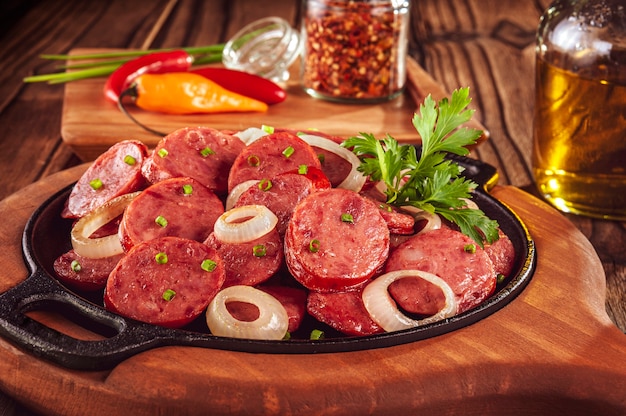 Sliced smoked calabrese sausage with onion in a wooden background - Brazilian appetizer close-up