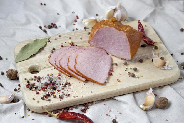 Sliced smoked meat on a wooden board with garlic and spices on a linen background close up