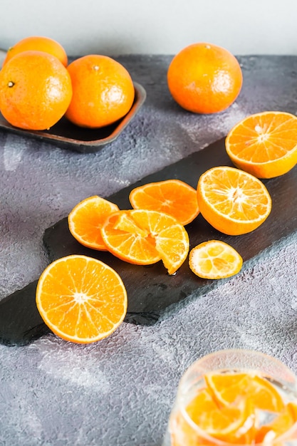 Sliced tangerines on a slate board and fresh fruits next to it on the table. Making cocktails. Vertical view