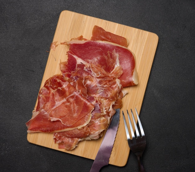 Sliced thin pieces of jamon on a wooden board black table