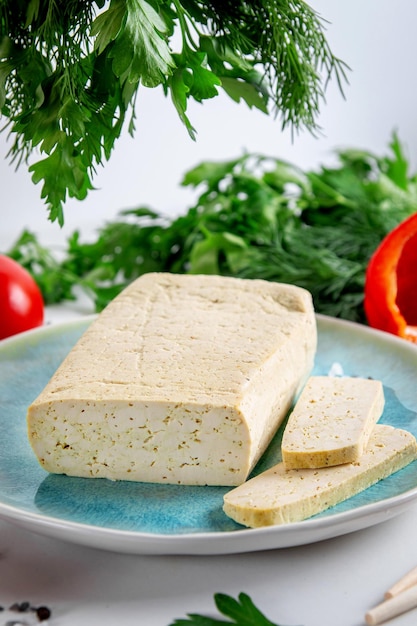 Sliced tofu soy cheese on a cutting board with basil spices and vegetables