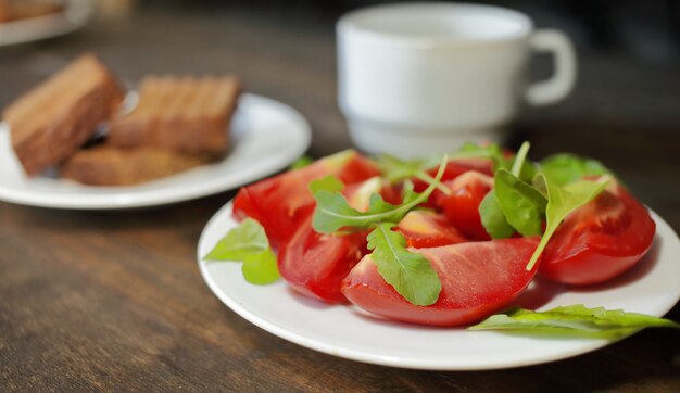 Sliced tomatoes with lettuce on a white plate and bread