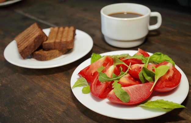 Sliced tomatoes with salad on a white plate with toast and a cup of coffee