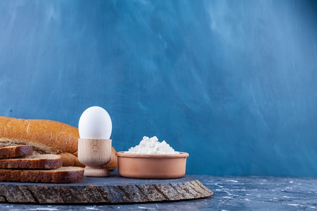 Sliced various bread, egg and bowl of flour on wood piece.