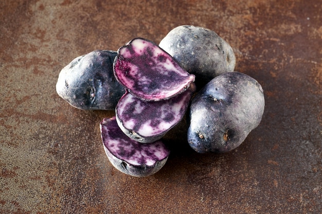 Sliced vitelotte potatos, three slices and three whole potatos on dark