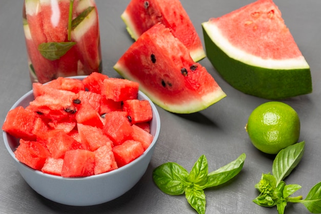 Sliced watermelon pulp in bowl Watermelon slices lime and sprig of basil on table