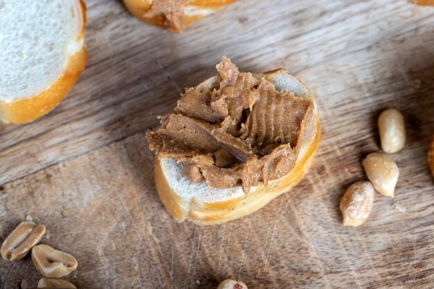 Sliced white bread with buttered peanut butter with pieces of crushed peanuts nut food on a cutting wooden board in the kitchen