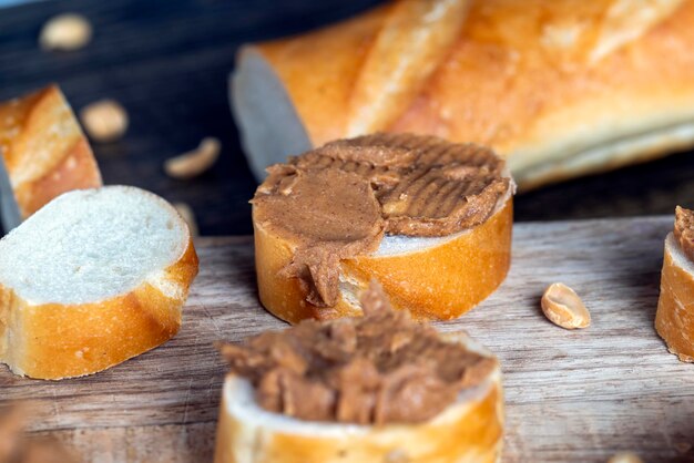 Sliced white bread with buttered peanut butter with pieces of crushed peanuts nut food on a cutting wooden board in the kitchen