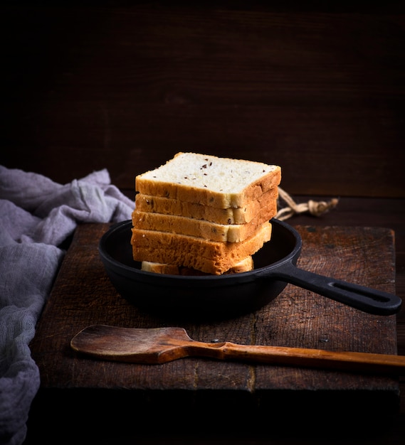 Slices of bread made of wheat flour in a round black cast-iron frying pan 