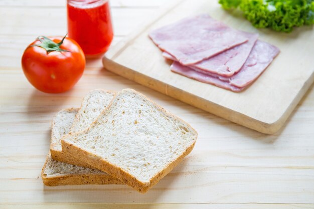 slices of bread with jam and ham, tamoto, lettuce,  on table with kitchen on table with kitchen