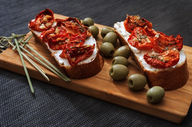 Slices of bread with sun-dried tomatoes and soft cheese, with green olives 