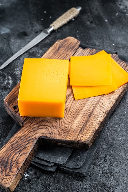 Slices of Cheddar Cheese on a wooden cutting board. black background. Top view.