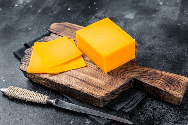 Slices of Cheddar Cheese on a wooden cutting board. black table . Top view.