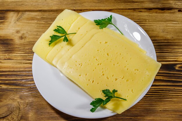 Slices of cheese in a plate on wooden table Top view