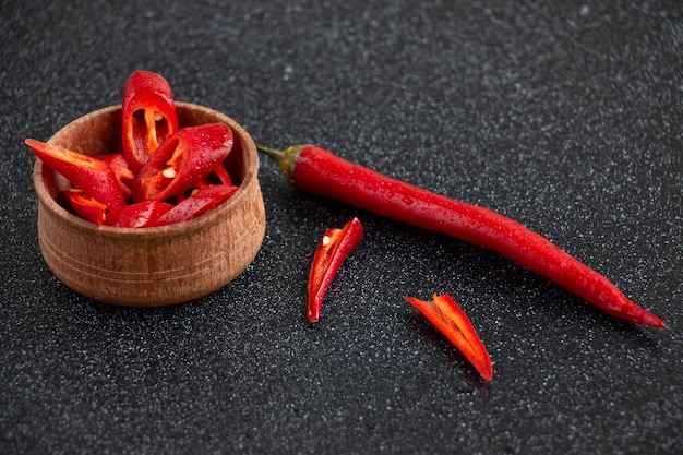 Slices of chili pepper and one whole pepper with water drops in the little wooden plate 