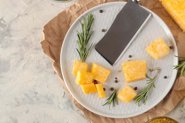 Slices of delicious marble cheese with a sprig of rosemary and cheese knife on a plate on a light concrete background. top view