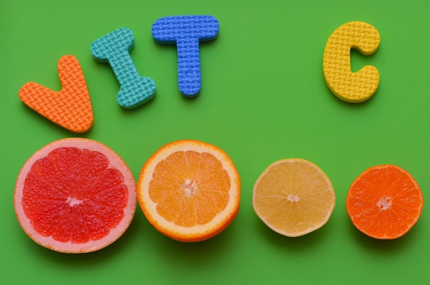 Slices of different types of citrus fruits and letters of the alphabet vitamin C on a green background closeup