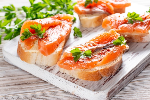 Slices of fresh baguette with butter and salmon served on wooden board on wood table