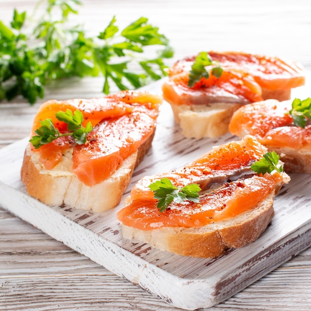 Slices of fresh baguette with butter and salmon served on wooden board on wood table