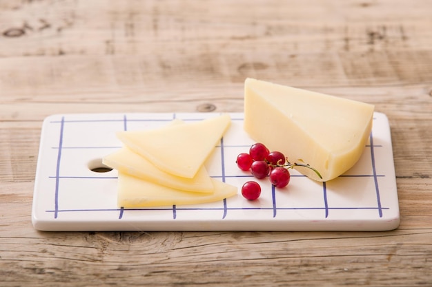 Slices of fresh homemade cheese served with red currant on rectangular plate on wooden background