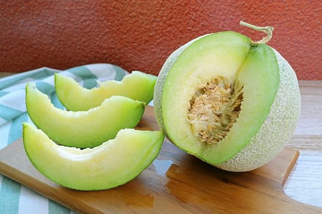 Slices of  Fresh Ripe Sweet and Aromatic Muskmelon with Whole Fruit on a Wooden Cutting Board