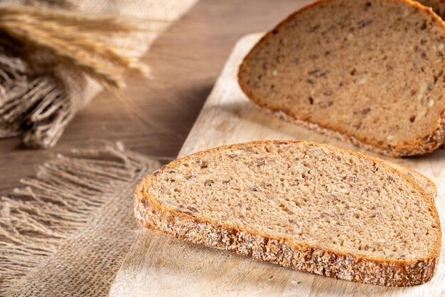 Slices of fresh rye bread with grains lie on the kitchen board in the background there are ears of barley and a burlap napkin closeup rustic style