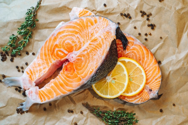 Slices of fresh salmon with lemon, black pepper and herbs on paper.