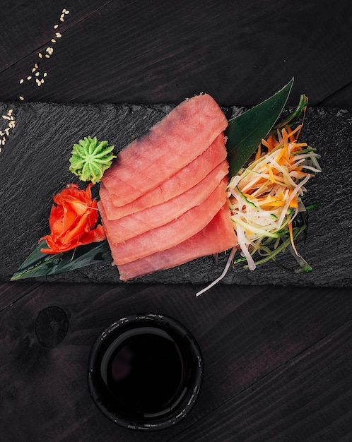 Photo slices of fresh tuna sashimi with soy sauce and wasabi on black stone plate