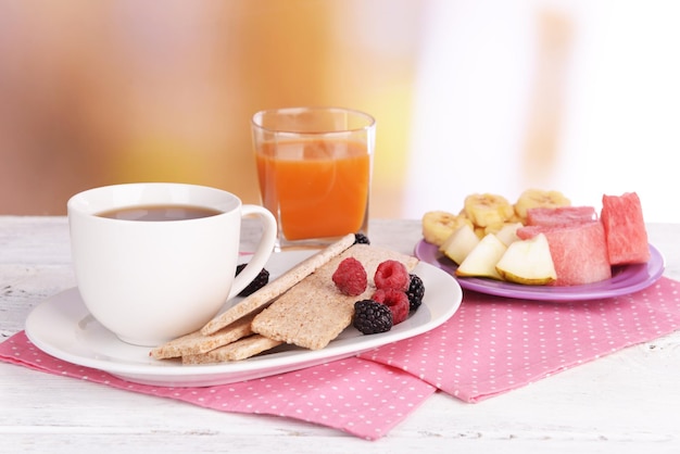 Slices of fruits with crispbreads and cup of tea on table on bright background