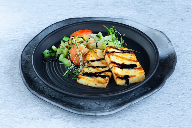 Slices of grilled halloumi cheese with vegetable salad, tomatoes and cucumber