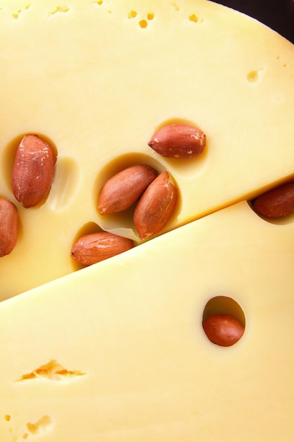 Slices of hard yellow cheese with nuts and berries on a black plate on a blue background Closeup of hard cheese slices with big holes