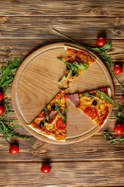 Slices Pizza on wooden board with tomatoes and basil Italian style on old wooden table top view