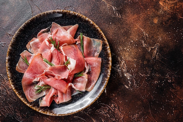 Slices of prosciutto crudo parma or jamon serrano with rosemary Dark background Top view Copy space