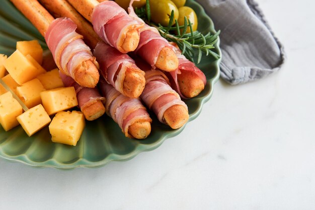 Slices of prosciutto or jamon Delicious grissini sticks with prosciutto cheese rosemary olives on green plate on dark background Appetizers table with italian antipasto snacks Top view copy space