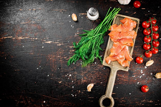 Slices of salted salmon on a cutting board with dill and tomatoes