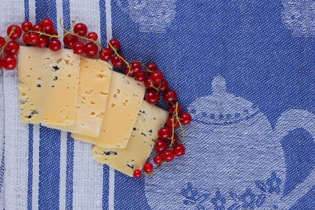 Slices of yellow hard cheese and red currants on a blue napkin Closeup of a healthy snack Healthy food concept View from above