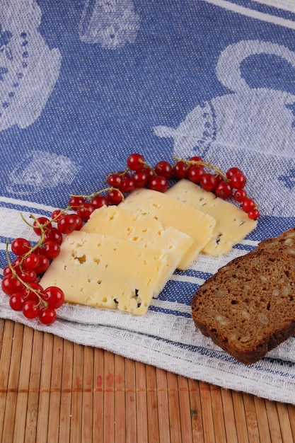 Slices of yellow hard cheese with red currants cucumber and grain bread on a blue napkin Closeup of a healthy snack Healthy food concept