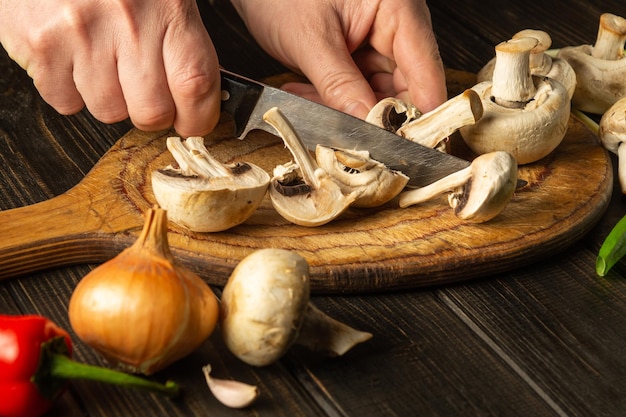 Slicing Agaricus mushrooms on cutting board by hands of chef using knife to prepare a delicious dish