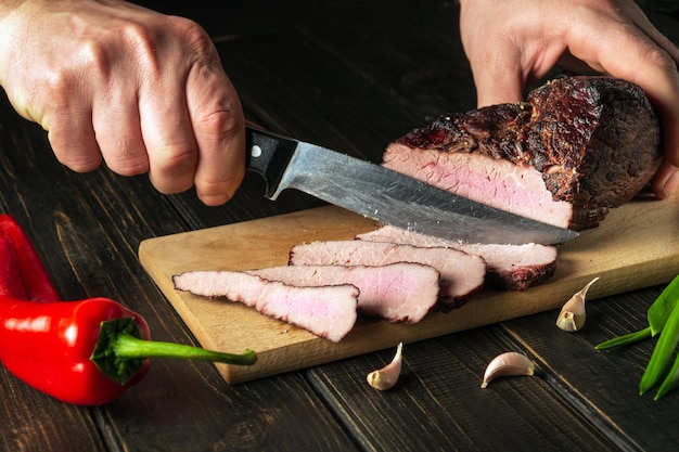 Slicing baked meat on a kitchen board Closeup of a chef hands with a knife European cuisine