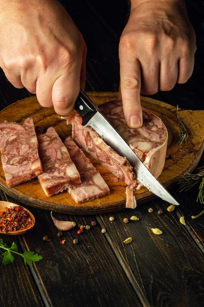 Slicing brawn on a cutting board with a knife in the hands of a cook Quick snack idea with headcheese with aromatic spices