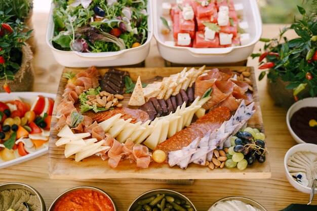 Slicing of cheeses and meat delicacies on the table with vegetable dishes and bitter pepper bushes