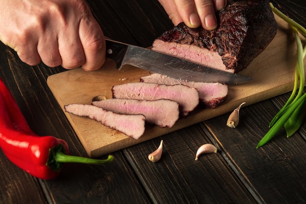 Slicing cooked meat on a kitchen board for dinner Closeup of a chef hands with a knife Peasant foods